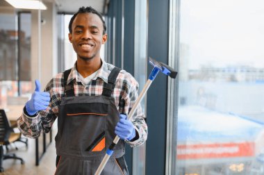 Afro-Amerikan üniformalı bir işçi camları silmek için cam sileceği kullanıyor, baş parmak işareti yapıyor, işinden memnun olduğunu gösteriyor.