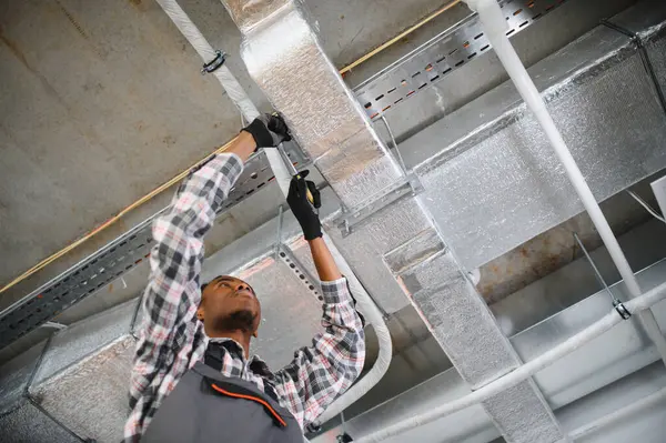 Genç Afro-Amerikan işçi bir havalandırma sistemi kuruyor, verimli hava akışı yönetimi için özel aletler ve ekipmanlar kullanıyor