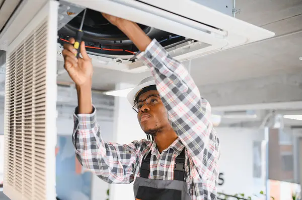 Afrikalı Amerikalı teknisyen modern bir binada bir havalandırma sistemini ustalıkla tamir ediyor. Hassasiyet ve teknik uzmanlık gösteriyor.