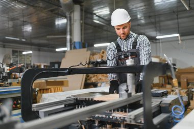 Marangoz, yoğun bir fabrika ortamında hassas ve uzman mobilya parçaları üreterek bir cnc makinesi çalıştırıyor.