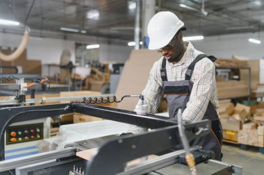 Odaklanmış Afro-Amerikan marangoz bir cnc makinesi çalıştırıyor, hareketli bir atölyede mobilya parçaları üretiyor.
