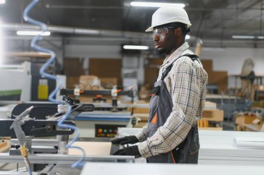 Marangoz, modern bir fabrikada mobilya üretimi için ahşap bir panel işliyor.