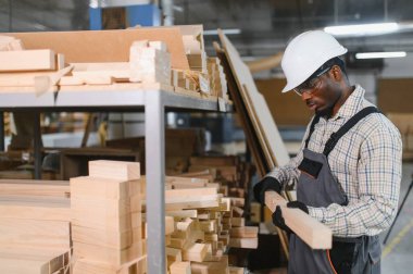 Marangoz güvenlik gözlüğü takıyor ve mobilya fabrikasında ahşap kalası inceliyor.