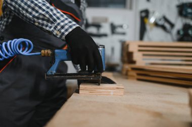 Marangoz, işlek bir mobilya fabrikasında pnömatik çivi tabancası kullanarak ahşap mobilya parçaları monte ediyor. Yetenekli işçilik ve hassasiyet sergiliyor.