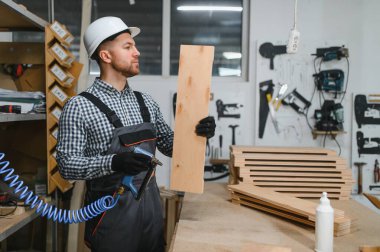 Marangoz ahşap kalasları inceliyor. Elinde pnömatik çivi tabancası var. Mobilya atölyesinde.