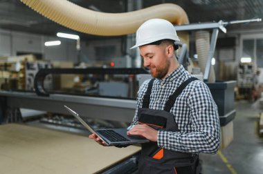 Mobilya fabrikasında çalışan işçiler, bilgisayar kullanarak cnc makinesini çalıştırıyor ve ahşap mobilya bileşenlerinin üretimini verimli bir şekilde arttırıyor.