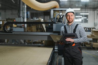 Marangoz, mobilya fabrikasındaki CNC ahşap yönlendirici makinesini çalıştırmak için dizüstü bilgisayar kullanıyor.