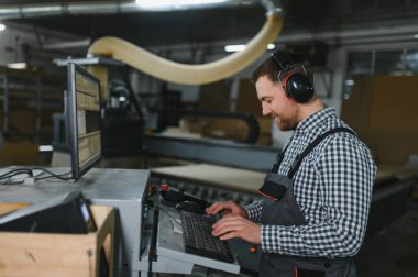 Mobilya fabrikasında çalışan bir işçi, cnc makinesiyle koltuklar için ahşap parçalar üretiyor, modern üretim tekniklerini sergiliyor.