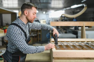 Marangoz ahşap bir kanepe çerçevesi monte ediyor. Mobilya fabrikasında pnömatik bir zımba tabancası var. Yetenekli bir işçilik ve hassasiyet sergiliyor.