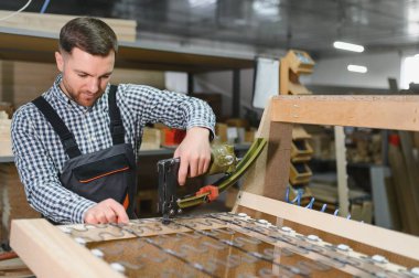 Marangoz mobilya fabrikasında çalışıyor ahşap kanepe iskeleti monte etmek için pnömatik zımba ve zig zag yayları kullanıyor.