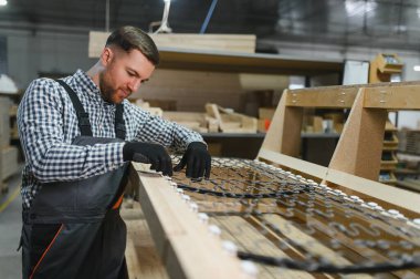 Marangoz, ahşap bir kanepe çerçevesine yaylar yerleştiriyor. Kaliteli işçilik ve konfor üzerine odaklanmış bir mobilya fabrikasında ustaca çalışıyor.