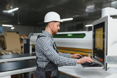 Modern bir mobilya fabrikasında güvenlik kaskı takan marangoz gelişmiş üretim süreçlerini sergiliyor.