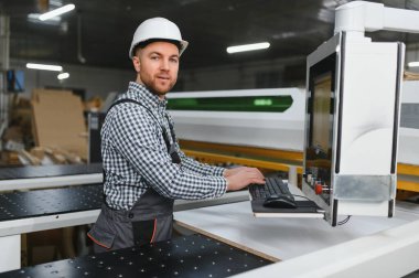 Mobilya fabrikasında güvenlik kaskı takan marangoz, üretim sürecini kontrol ediyor.