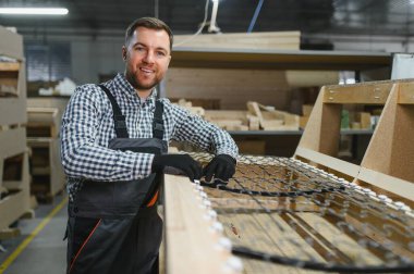 Marangoz, hareketli bir mobilya fabrikasında metal yaylarla entegre edilmiş ahşap bir kanepe çerçevesi monte ediyor. Yetenekli işçilik ve detaylara dikkat gösteriliyor.