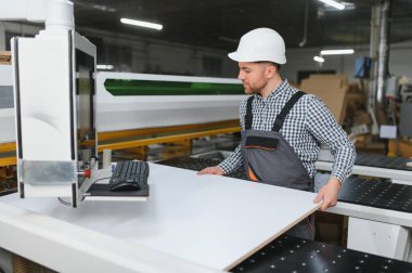 Marangoz bir mobilya fabrikasında cnc makinesine ahşap tahta yerleştiriyor, modern marangozluk teknolojisini sergiliyor.