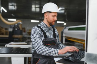 Marangoz güvenlik kaskı takıyor. Mobilya fabrikasında bilgisayar klavyesi kullanıyor.