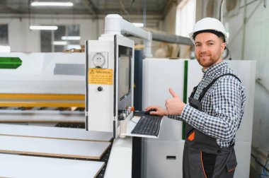 Marangoz, bir mobilya fabrikasında CNC makinası çalıştırıyor ve memnuniyetini göstermek için başparmağını kaldırıyor.