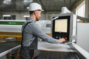 Bir mobilya fabrikasında güvenlik kaskı takan marangoz, üretim sürecini kontrol ediyor.