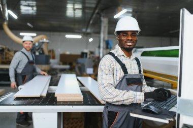 Marangozlar bir mobilya fabrikasında ahşap paneller ve bilgisayar sayısal kontrol makinesiyle çalışıyorlar.