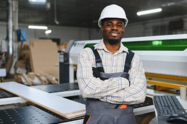 Bir mobilya fabrikasında CNC makinelerini yöneten Afro-Amerikan işçisi, kanepe üretimi için odun üretimine odaklanıyor.