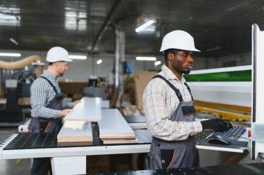 İki marangoz, bir cnc makinesi üzerinde çalışıyor. Hareketli bir mobilya fabrikasında ustalıkla ahşap döşeme şekillendiriyorlar.