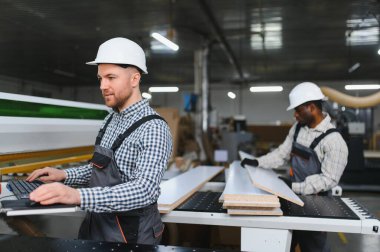 Cnc makinesinde çalışan iki marangoz, mobilya fabrikasında ahşap tahtaları ustalıkla kesiyorlar.