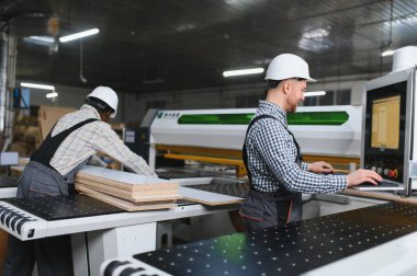 Marangozlar modern bir cnc makinesini ustalıkla işletiyorlar, hareketli bir mobilya fabrikasında ahşap paneller kesiyorlar, hassasiyet ve takım çalışması sergiliyorlar.