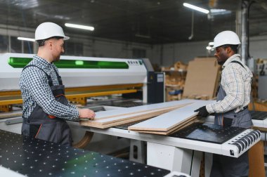 İki marangoz aktif bir mobilya fabrikasında cnc makinesinin yanında çalışırken ahşap tahtalar üzerinde iş birliği yapıyorlar.