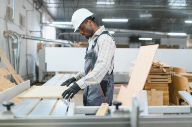 Profesyonel marangoz, yoğun mobilya fabrikasında kesin kesim ve şekillendirme için modern cnc makinesine ahşap panel dikkatlice yerleştiriyor.