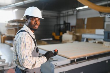 Kanepe üretimi için hassas ahşap kesimine odaklanan, bir mobilya fabrikasında cnc makinesini yöneten Afrikalı Amerikalı işçi.