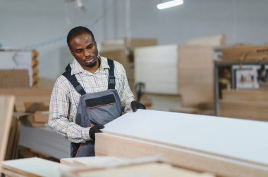Marangoz, bir mobilya fabrikasında ahşap tahtaları dikkatlice seçerek üretim kalitesini sağlama alıyor.