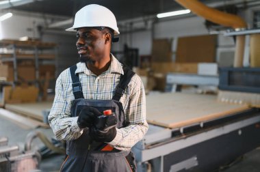 Marangoz, bir mobilya fabrikasında CNC makinesini kontrol ediyor. Modern ahşap işçiliğinde uzmanlık ve hassasiyet sergiliyor.