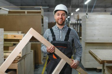 Gülümseyen marangoz ahşap bir çerçeve tutarken çalışkan bir mobilya fabrikasında çalışarak, işçilik ve beceri sergileyerek