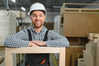 Ağaç çerçeveye yaslanmış gülümseyen bir marangozun portresi, mobilya fabrikasında zanaat ve gurur sergiliyor.