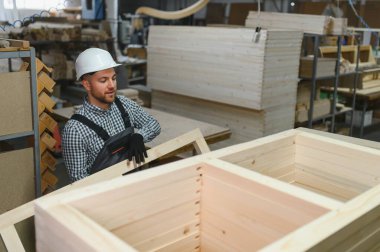 Mobilya fabrikasında çalışan bir işçi ahşap bir kanepe çerçevesi kuruyor. Etrafı malzeme ve aletlerle çevrili. İşçilik ve üretim sürecine odaklan