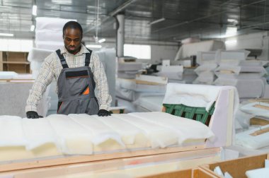 Afro-Amerikan işçiler bir mobilya fabrikasında kanepe monte ediyorlar. Etrafı malzeme ve makinelerle çevrili. Endüstriyel işçilik sergiliyorlar.