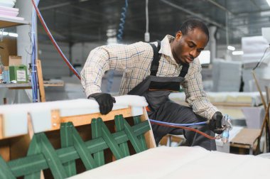 Koltuk çerçevesinde tutkal tabancası kullanan usta bir zanaatkar mobilya üretiminde döşeme teknikleri gösteriyor.