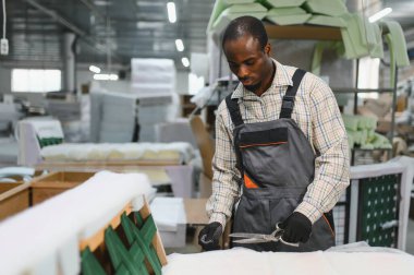 Mobilya fabrikasında kanepe yapımında çalışan yetenekli bir zanaatkar büyük bir makasla kumaşı dikkatlice kesiyor.