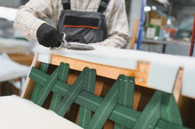 Bir mobilya fabrikasında yüksek kaliteli döşeme yapmak için makas ve çeşitli aletler kullanan bir zanaatkar özenle bir koltukta çalışıyor.