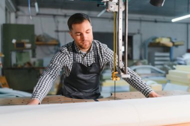 Marangoz dikey bir testereyi dikkatlice çalıştırıyor, mobilya döşemeleri için beyaz kumaş kesiyor.