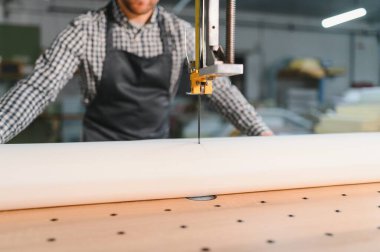 Marangoz önlük giyip testereyle mobilya fabrikasında beyaz dolgu malzemesi kesiyor.
