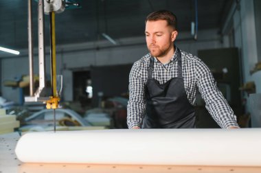 Marangoz, bir mobilya fabrikasındaki bir cnc makinesinde işlem için malzeme hazırlıyor, hassasiyet ve kaliteli işçilik üzerine odaklanıyor.