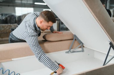 Marangoz bir mobilya fabrikasında kanepe monte ediyor, vidaları sıkmak için pnömatik tornavida kullanıyor.