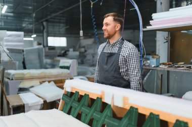 Marangoz gülümsüyor ve mobilya fabrikasında bir kanepede çalışıyor, ahşap ve diğer malzemeleri kullanarak.