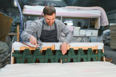 Marangoz pnömatik zımba tabancası kullanıyor, mobilya atölyesindeki ahşap kanepe çerçevesini tamir ediyor.