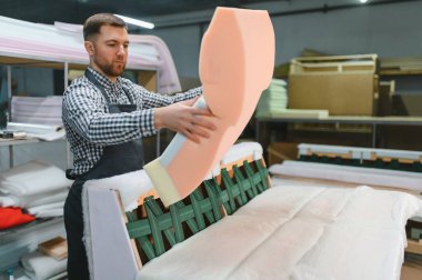 Marangoz mobilya fabrikasında kanepe montajı, ahşap çerçeveye köpük yerleştirme, döşenmiş mobilya üretim süreci