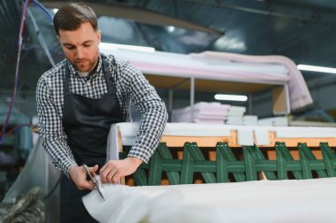 Marangoz kumaş kesiyor ve mobilya fabrikasında alet ve malzeme kullanarak kanepe çerçevesinde çalışıyor.