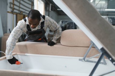 Mobilya fabrikasında bir koltukta çalışan yetenekli bir zanaatkar çerçeveyi monte etmek ve kaliteyi sağlamak için elektrikli bir alet kullanıyor.