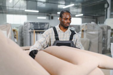 Afrikalı Amerikalı işçiler, iyi aydınlatılmış bir alanda, sarılı mobilya ve makinelerle çevrili bir mobilya üretim tesisinde bir kanepeyi inceliyor.