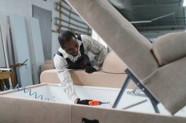 Marangoz yoğun bir mobilya fabrikasında bej bir kanepe monte ediyor, döşeme ustalığı sergiliyor.